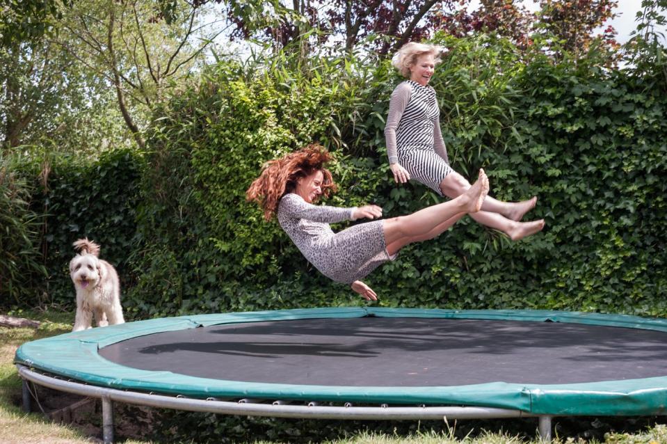 Two adults playing on a trampoline. A dog is watching.