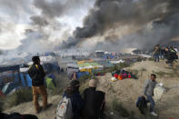 Smoke rises the sky as migrants and journalists look at burning makeshift shelters and tents in the "Jungle" on the third day of their evacuation and transfer to reception centers in France, as part of the dismantlement of the camp in Calais, France. REUTERS/Philippe Wojazer