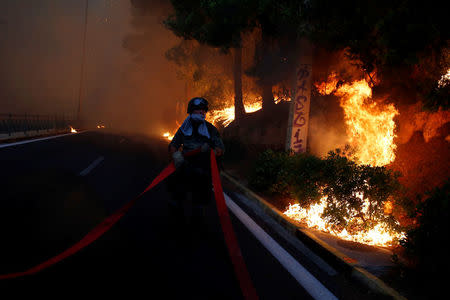 A soldier holds a hose as a wildfire burns in the town of Rafina, near Athens, Greece, July 23, 2018. REUTERS/Costas Baltas