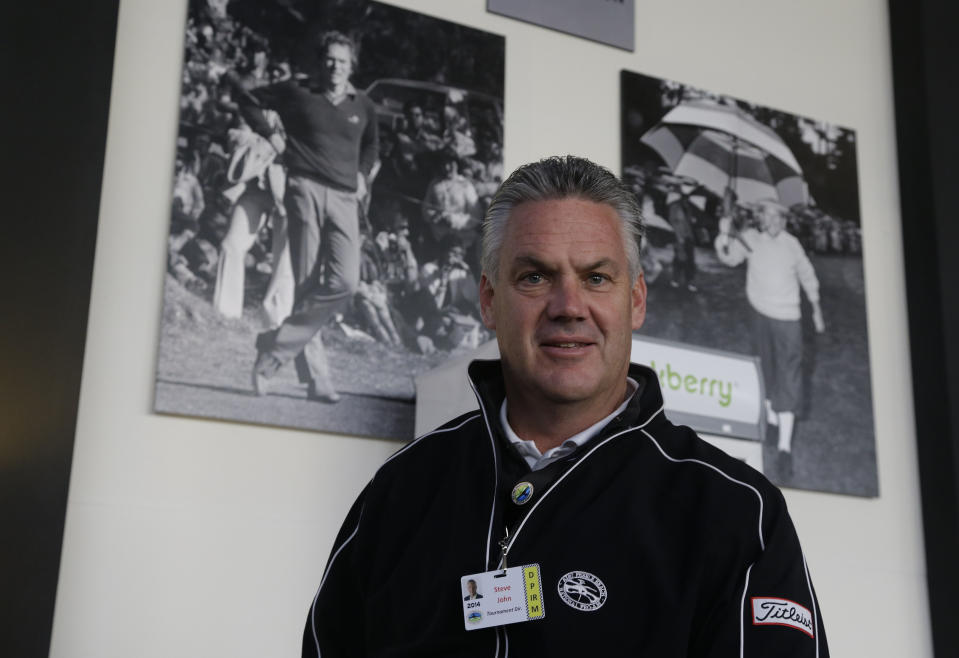 Steve John, CEO of the Monterey Peninsula Foundation and tournament director of the AT&T Pebble Beach Pro-Am golf tournament, poses beneath photographs of Clint Eastwood, left, and Bing Crosby, right, Friday, Feb. 7, 2014, in Pebble Beach, Calif. John was choking on a piece of cheese at a volunteer party when Eastwood gave him the Heimlech maneuver, Wednesday evening, Feb. 5, 2014, at the Monterey Conference center in Monterey, Calif. (AP Photo/Eric Risberg)