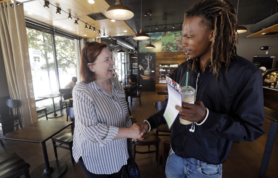 In this photo taken Monday, June 10, 2019, Seattle City Council candidate Pat Murakami, left, greets voter James Williams at a coffee shop in Seattle. A first-of-its-kind public campaign finance program in Seattle gives voters vouchers worth $100 to pass on to any candidate they want. Now in its second election cycle, advocates say the program can level the political playing field, although its first round in Seattle showed mixed results. (AP Photo/Elaine Thompson)