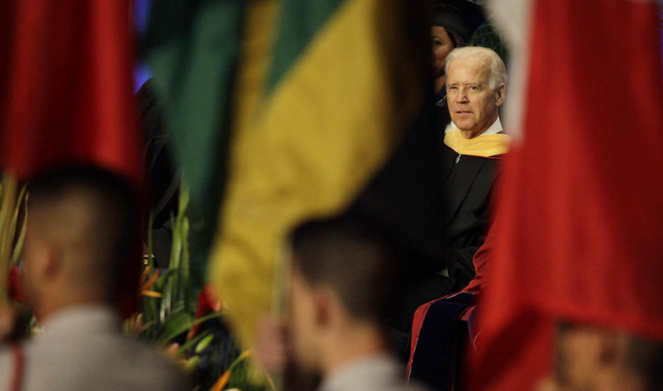 A procession with International flags past as Vice President Joe Biden listens during a graduation ceremony at the Miami Dade College in Miami, Saturday, May 3,2014. Biden said a "constant, substantial stream of immigrants" is important to the American economy, urging citizenship for immigrants living in the U.S. illegally. (AP Photo/Javier Galeano)