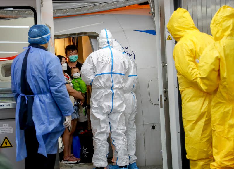 Workers in protective suits await passengers from a Xiamen Airlines airplane as they get off the charter flight sent by the Chinese government to bring home Hubei residents from Thailand's Bangkok, at Wuhan Tianhe International Airport