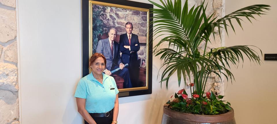 Award-winning server Dolly Punwasi posing by a portrait of hotel founders J. Willard Marriott and his son, J.W. Jr.