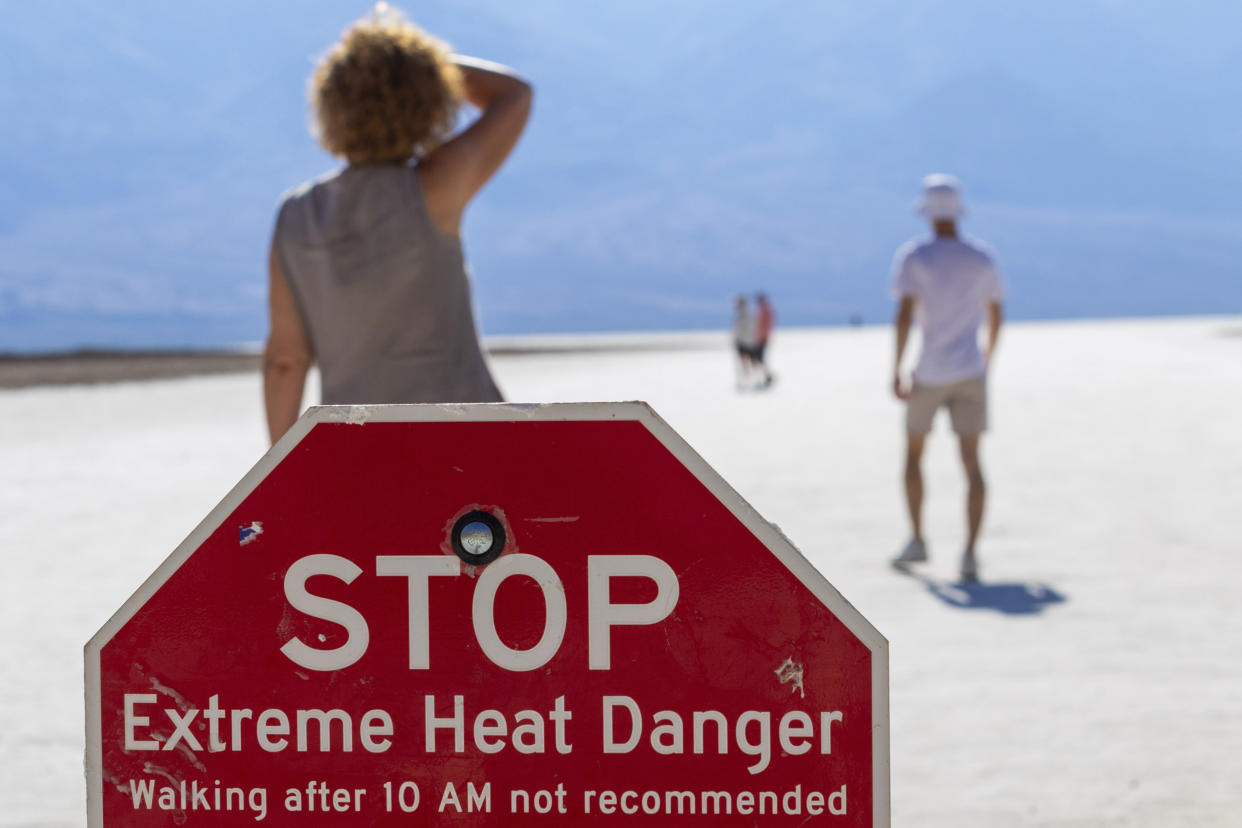 A person wipes sweat from their brow at Badwater Basin in Death Valley National Park on Sunday, behind a read sign reading 