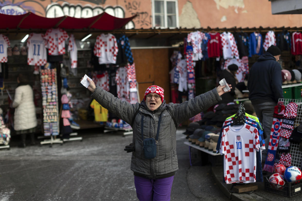 A woman wearing a checkered hat in the colors of the Croatian coat of arms cheers as she walks through a market ahead of the national team's Qatar World Cup soccer semifinal match against Argentina, in Zagreb, Croatia, Tuesday, Dec. 13, 2022. (AP Photo/Marko Drobnjakovic)