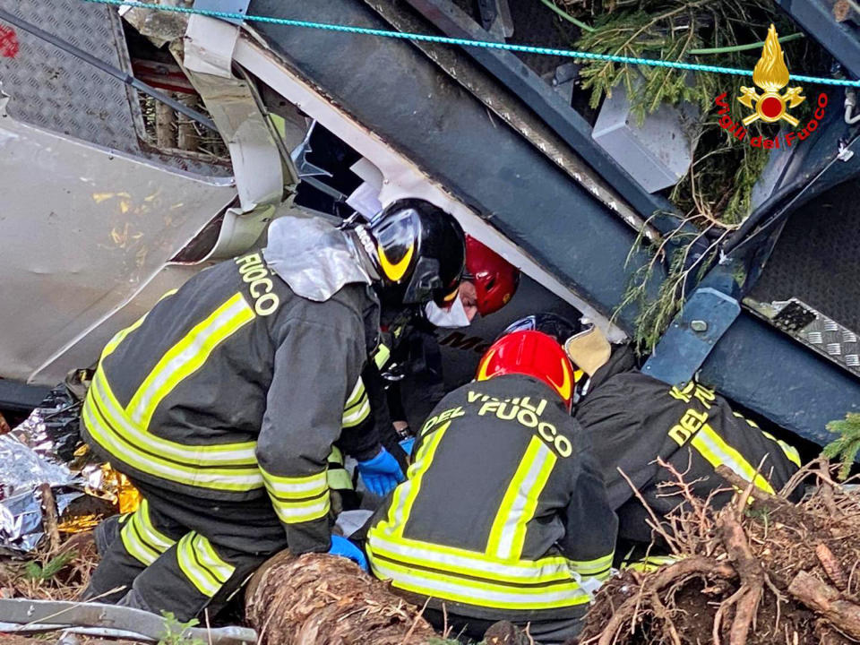 Rescuers work by the wreckage of a cable car after it collapsed near the summit of the Stresa-Mottarone line in the Piedmont region, northern Italy, Sunday, May 23, 2021. A cable car taking visitors to a mountaintop view of some of northern Italy's most picturesque lakes plummeted to the ground Sunday and then tumbled down the slope, killing at least 13 people and sending two children to the hospital, authorities said. (Italian Vigili del Fuoco Firefighters via AP)