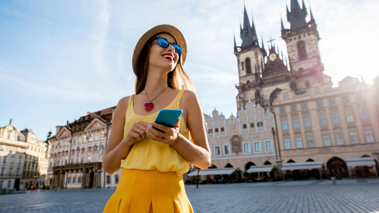  Young woman in yellow walking with smart phone on the old town square in Prague city 