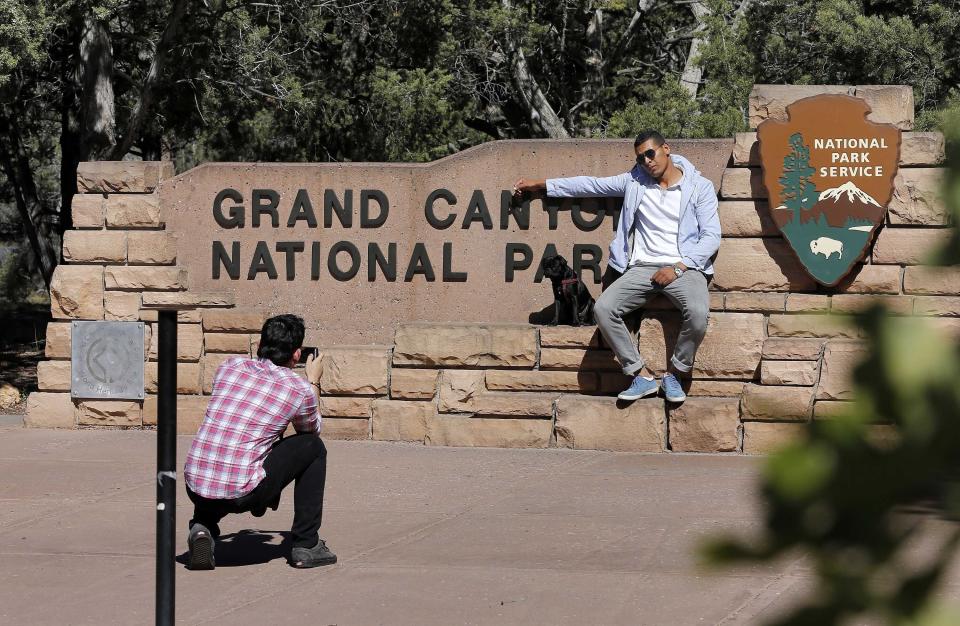 FILE - Ahmed Alaawaj, of Libya, gets his photo taken by Juan Riaz, of Colombia, at the Grand Canyon National Park entrance in Tusayan, Ariz., October 2013. The friends traveled from Las Vegas to see the Grand Canyon unknowing it was shut down. Arizona's Grand Canyon National Park and all five national parks in Utah will remain open if the U.S. government shuts down, Sunday, Oct. 1, 2023. Arizona Gov. Katie Hobbs and Utah Gov. Spencer Cox say that the parks are important destinations and local communities depend on dollars from visitors. (AP Photo/Matt York, File)