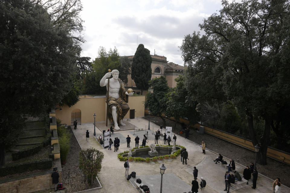 Visitors admire a massive, 13-meter (yard) replica of the statue Roman Emperor Constantine commissioned for himself after 312 AD that was built using 3D technology from scans of the nine giant original marble body parts that remain, as it was unveiled in Rome, Tuesday, Feb. 6, 2024. The imposing figure of a seated emperor, draped in a gilded tunic and holding a scepter and orb, gazing out over his Rome, is located in a side garden of the Capitoline Museums, just around the corner from the courtyard where the original fragments of Constantine's giant feet, hands and head are prime tourist attractions. (AP Photo/Andrew Medichini)