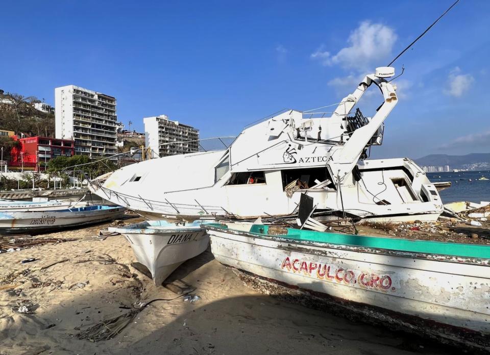 A wrecked yacht next to a fishing boat on the beach.