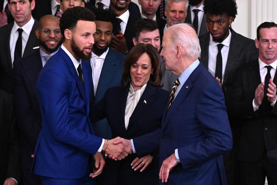 US President Joe Biden (R) shakes hands with Golden State Warriors basketball player Stephen Curry (L)  as US Vice President Kamala Harris (C) looks on during a celebration for the Golden State Warriors 2022 NBA championship at the White House in Washington, DC, on January 17, 2023.