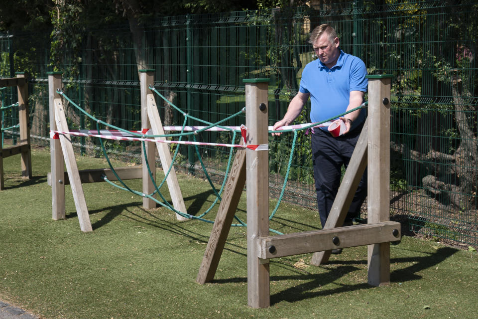 Head teacher Graham Hamilton tapes off playground equipment as measures are taken to prevent the transmission of coronavirus before the possible reopening of Lostock Hall Primary school in Poynton near Manchester, England, Wednesday May 20, 2020. (AP Photo/Jon Super)