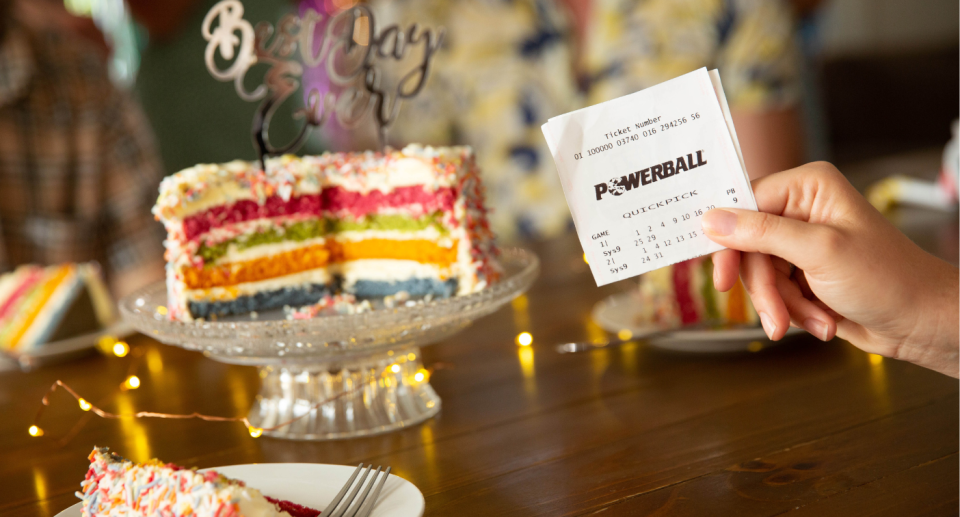 A person holds up a Powerball ticket in front of a cake.