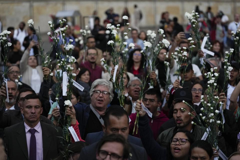 People hold flowers during an event to remember former guerrillas and social leaders who have been killed since the 2016 signing of a peace agreement between rebels of the Revolutionary Armed Forces of Colombia, FARC, and the government, in Bogota, Colombia, Tuesday, Feb. 20, 2024. (AP Photo/Fernando Vergara)