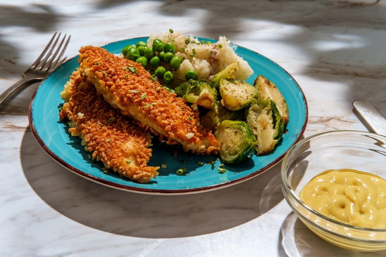 Country style chicken fingers mashed potatoes brussels sprouts peas on plate and honey mustard for dipping