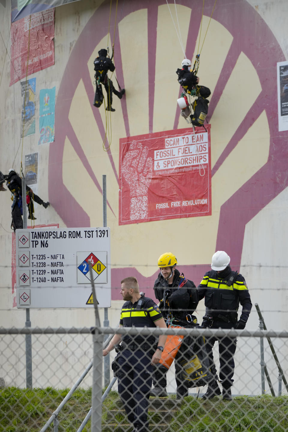 A handcuffed Greenpeace climate activist, wearing a yellow helmet, is led away by police after being lowered from a fuel storage tank during a protest at a Shell refinery in Rotterdam, Netherlands, Monday, Oct. 4, 2021. A coalition of environmental groups launched a campaign calling for a Europe-wide ban on fossil fuel advertising ahead of the United Nations Climate Change Conference, also known as COP26, which start in Glasgow on Oct. 31st, 2021. (AP Photo/Peter Dejong)