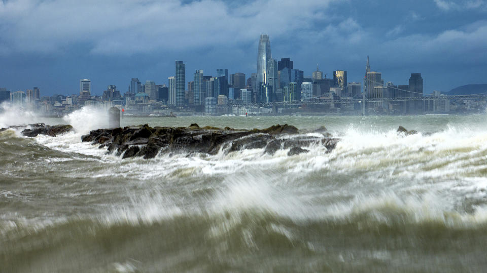 Waves crash over a breakwater in Alameda, Calif., with the San Francisco skyline in the background on Sunday, Feb. 4, 2024. High winds and heavy rainfall are impacting the region. (AP Photo/Noah Berger)