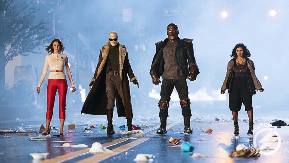 A still from the first season of Doom Patrol shows Rita Farr, Negative Man, Robot Man, and Crazy Jane standing on a road looking shocked