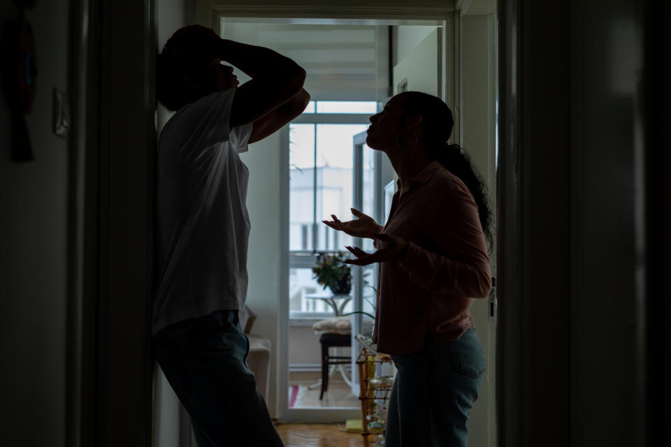 A man and woman are arguing intensely in a dimly lit hallway, both displaying frustrated and upset body language