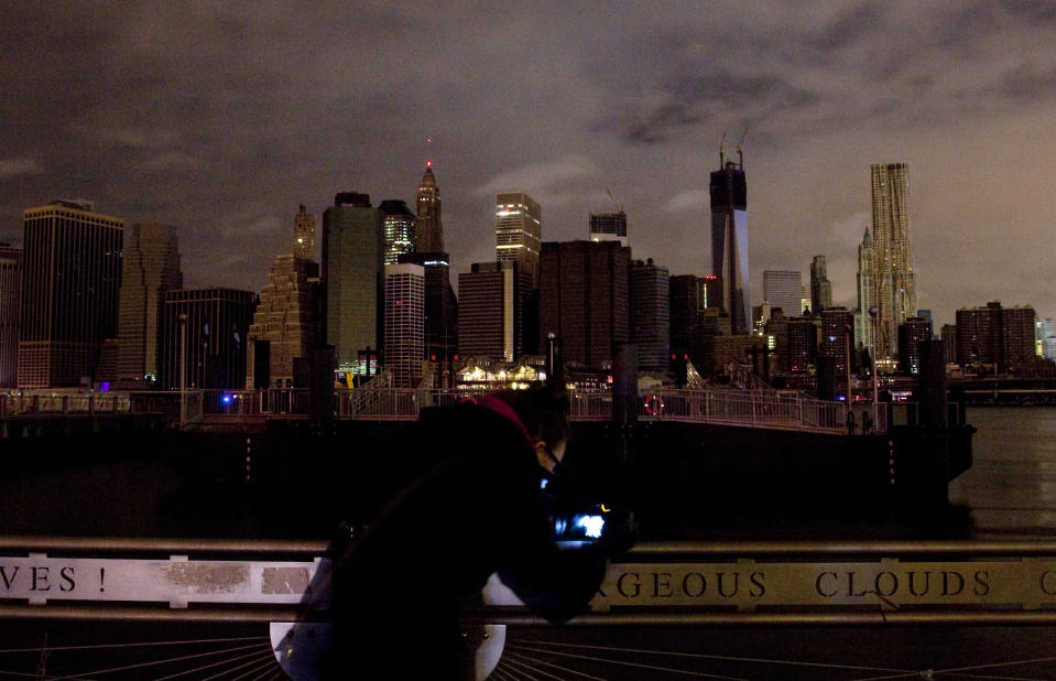 A woman photographs the Manhattan skyline, Tuesday, Oct. 30, 2012 in New York. Much of lower Manhattan is without electric power following the impact of superstorm Sandy. (AP Photo/Mark Lennihan)