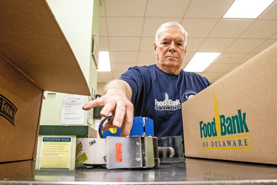 David Snyder, a volunteer for three and a half years at the Food Bank of Delaware, reaches for the tape in the volunteer room of the Food Bank in Milford, Friday, Nov. 10, 2023.