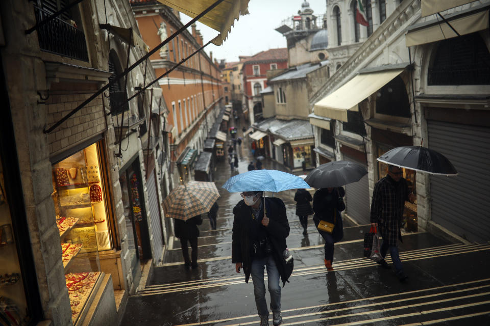 People shelter against the rain with umbrellas as they walk along the Rialto bridge on a rainy day in Venice, Sunday, March 1, 2020. In northern Italy, the virus COVID-19 is taking a deep social toll, curtailing the usual opportunities to meet. (AP Photo/Francisco Seco)