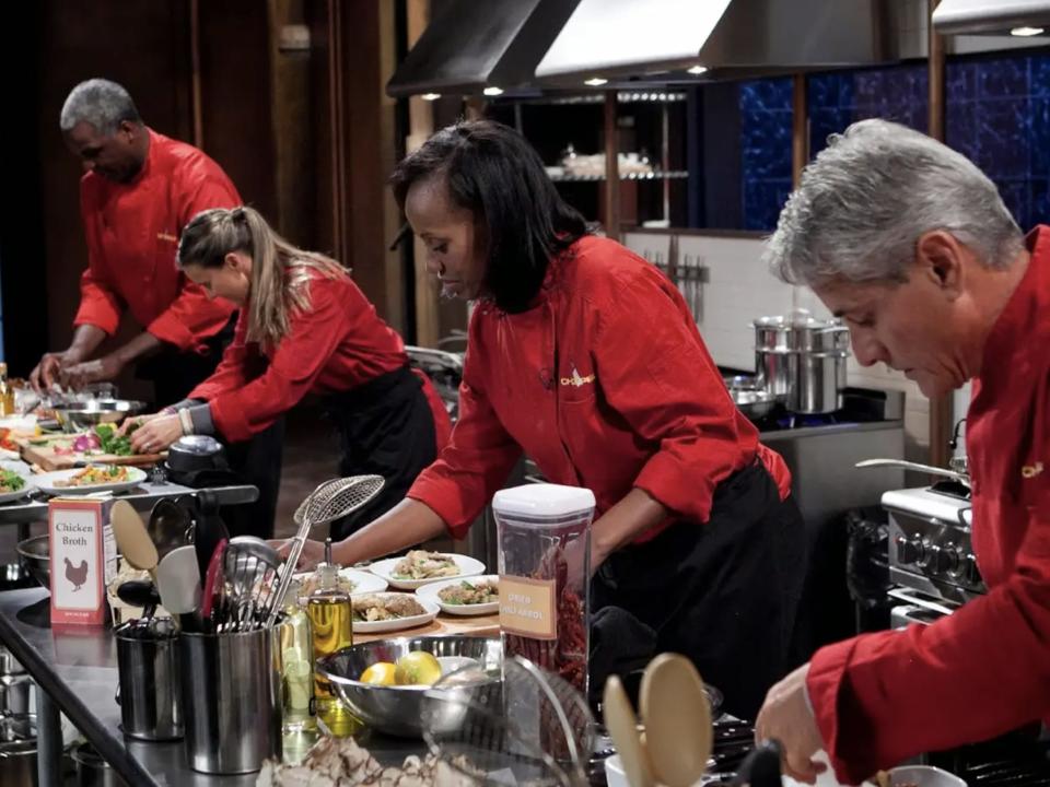 "Chopped" chefs in red coats at each station cooking during round