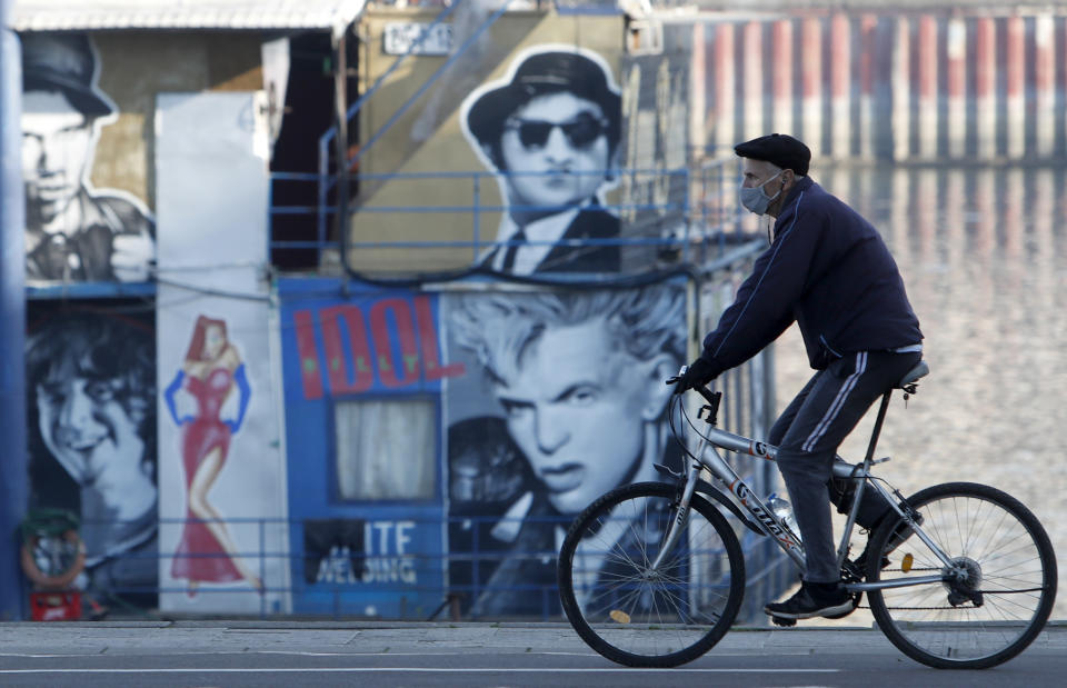 A man wearing a fask mask to protect against coronavirus, rides a bicycle by a closed raft restaurant on the banks of Sava river during a sunny, wintery day in Belgrade, Serbia, Wednesday, Dec. 23, 2020. (AP Photo/Darko Vojinovic)