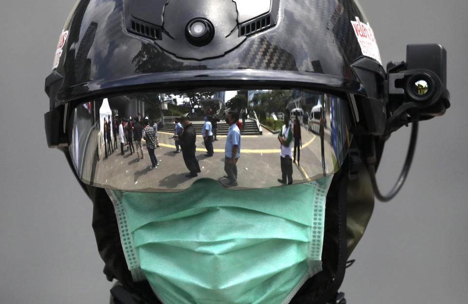 The reflection of people queuing to be tested for the coronavirus is seen on the visor of a medical official outside a mobile test site in Jakarta, Indonesia, Wednesday, May 6, 2020. The Indonesian government has postponed Sept. 23, 2020, regional elections until at least December this year due to the pandemic. (AP Photo/Dita Alangkara)