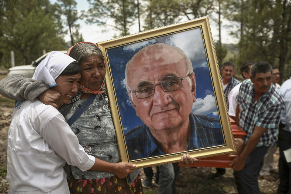 FILE - Women hold a portrait of Jesuit priest Javier Campos Morales as his funeral procession and that of fellow priest Joaquin Cesar Mora Salazar arrives to Cerocahui, Chihuahua state, Mexico, Sunday, June 26, 2022, after the the two elderly priests and a tour guide were murdered in Mexico's Sierra Tarahumara. Two months after a pair of Jesuit priests were killed in a remote mountain community in northern Mexico, the suspected killer remains on the loose and townspeople are frightened, but the religious order says it is not leaving. (AP Photo/Christian Chavez, File)