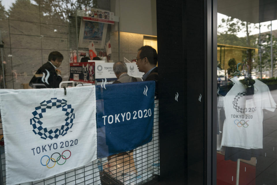 FILE - In this June 19, 2019, file photo, people shop at a store selling Olympic souvenirs in Tokyo. Scandals and rising costs have not deterred interest in Japan in the Tokyo Olympic. They open in a year with unprecedented ticket demand. (AP Photo/Jae C. Hong, File)