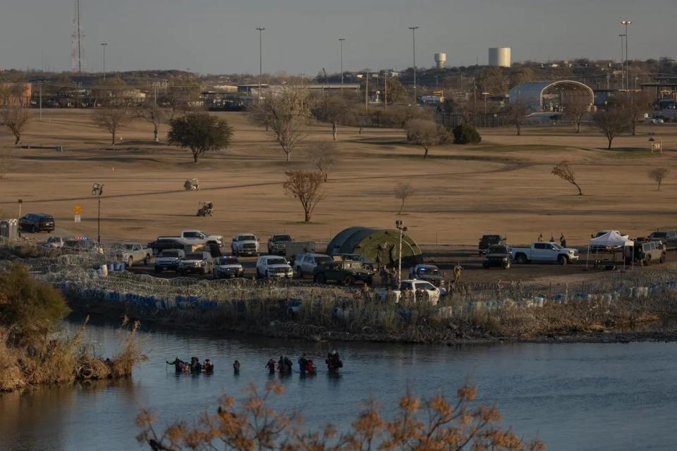 A group of migrants wades through the Rio Grande under the watch of Texas National Guard members near the riverbank at Shelby Park in Eagle Pass on Jan. 19, 2024. Texas has closed off Shelby Park, cutting access to federal agents to part of the Texas-Mexico border, according to a federal legal filing. The situation is escalating tensions between the Biden administration and Gov. Greg Abbott.