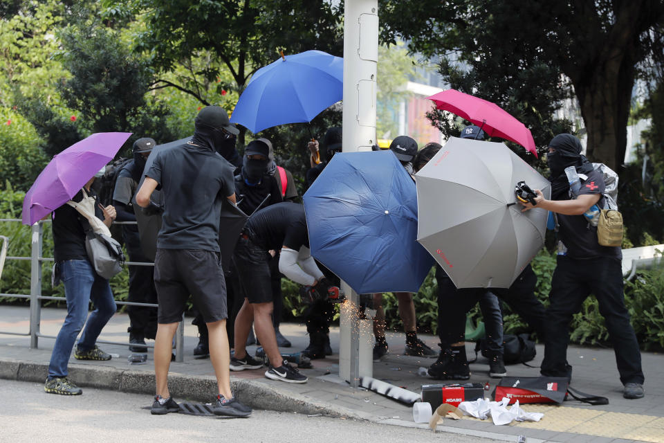 FILE - Demonstrators use umbrellas to shield themselves from view while they try to cut down a smart lamppost during a protest in Hong Kong, Saturday, Aug. 24, 2019. On Friday, May 6, 2022, The Associated Press reported on stories circulating online incorrectly claiming a video shows people in Hong Kong “rebelling against the COVID police state by cutting down and destroying security cameras.”(AP Photo/Kin Cheung, File)