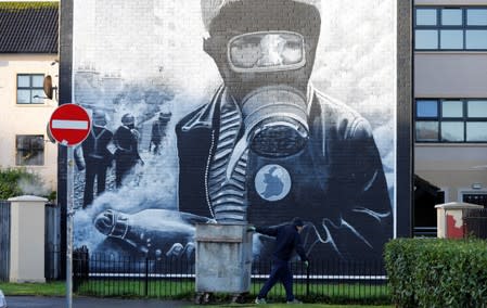 A man pulls a rubbish bin past a mural in the Bogside area of Londonderry, Northern Ireland