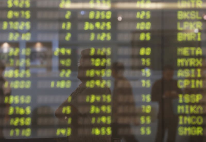 A man stands near electronic board showing stock market index at Bank Mandiri Sekuritas trading floor in Jakarta