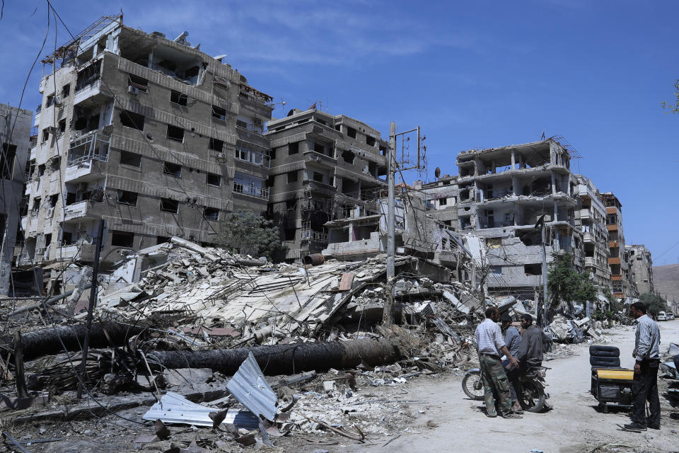 FILE - People stand in front of damaged buildings, in the town of Douma, the site of a suspected chemical weapon attack, near Damascus, Syria, on April 16, 2018. Syria on Thursday Feb. 2, 2023 dismissed the findings of an investigation of which the global chemical weapons watchdog concluded that there were "reasonable grounds to believe" Syria's air force dropped two cylinders containing chlorine gas on the city of Douma in 2018. Syria denies ever using chemical weapons during the war and says it eliminated its chemical arsenal under a 2013 agreement brokered by the U.S. and key ally Russia. It also joined the Hague-based global chemical weapons watchdog as global pressure mounted on Damascus.(AP Photo/Hassan Ammar, File)