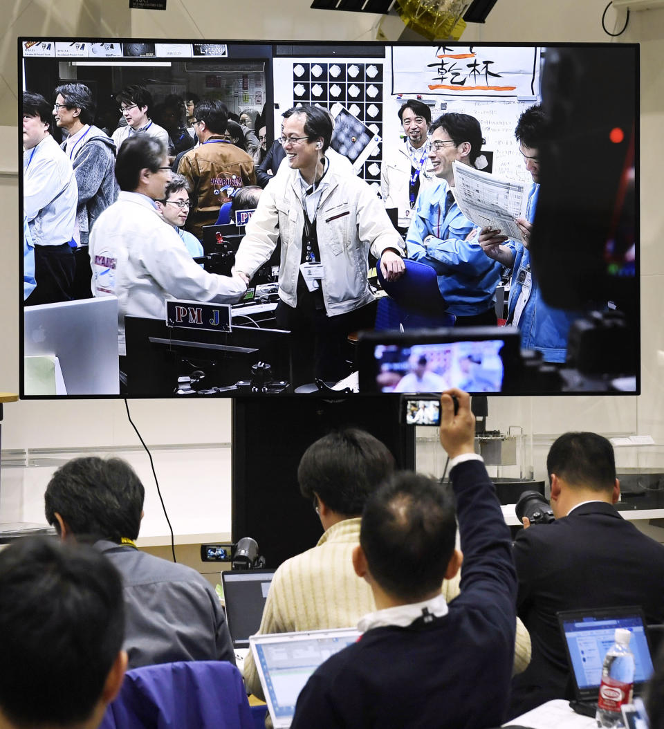 Members of The Japan Aerospace Exploration Agency, or JAXA, seen on screen, celebrate, as Hayabusa2 spacecraft safely evacuated and remained intact after the blast, in Sagamihara, near Tokyo, Friday, April 5, 2019. Japan's space agency says its spacecraft has released an explosive onto an asteroid to make a crater on its surface and collect underground samples to find possible clues to the origin of the solar system. (Daisuke Suzuki/Kyodo News via AP)