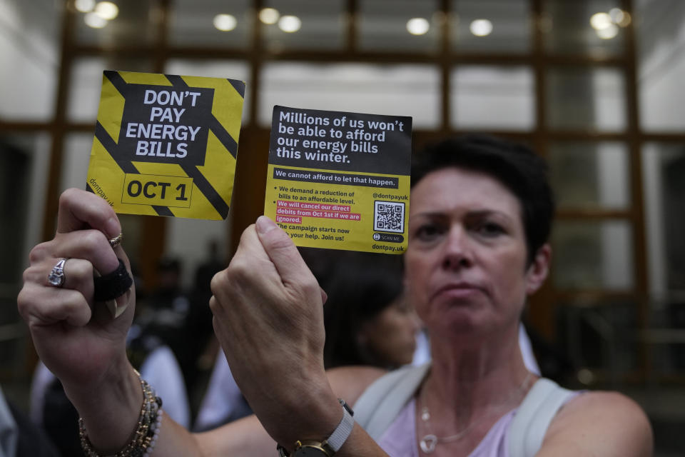 FILE - A demonstrator holds up two cards as they protest outside the British energy regulator Ofgem, which put up the price cap for gas and electricity by around 80 per cent for most households, in London, Friday, Aug. 26, 2022. Britain's energy regulator said Thursday that the typical household energy bill will come down by around 400 pounds ($495) a year from July as global wholesale energy prices come down. (AP Photo/Alastair Grant, File)