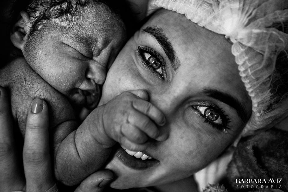 A newborn grabs his mother's nose as she smiles for the camera