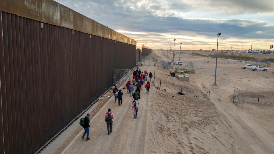 Immigrants walk along the U.S.-Mexico border wall after crossing the Rio Grande into El Paso, Texas on February 1, 2024. - John Moore/Getty Images