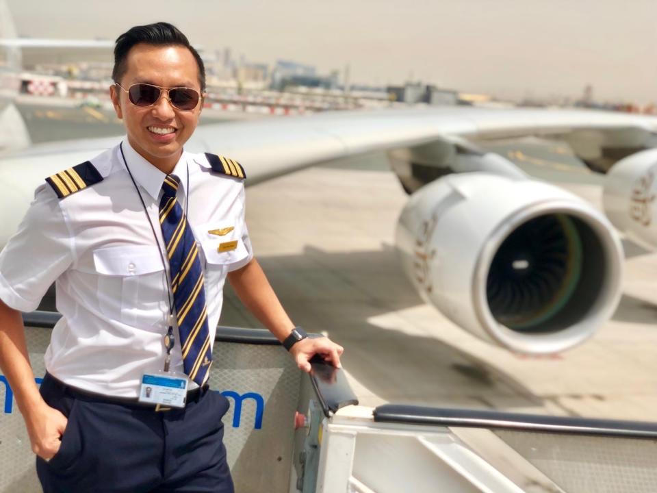 Yursi Abu Barak, who is wearing a pilot uniform and a pair of tinted sunglasses, poses on the passenger entrance to an airplane.