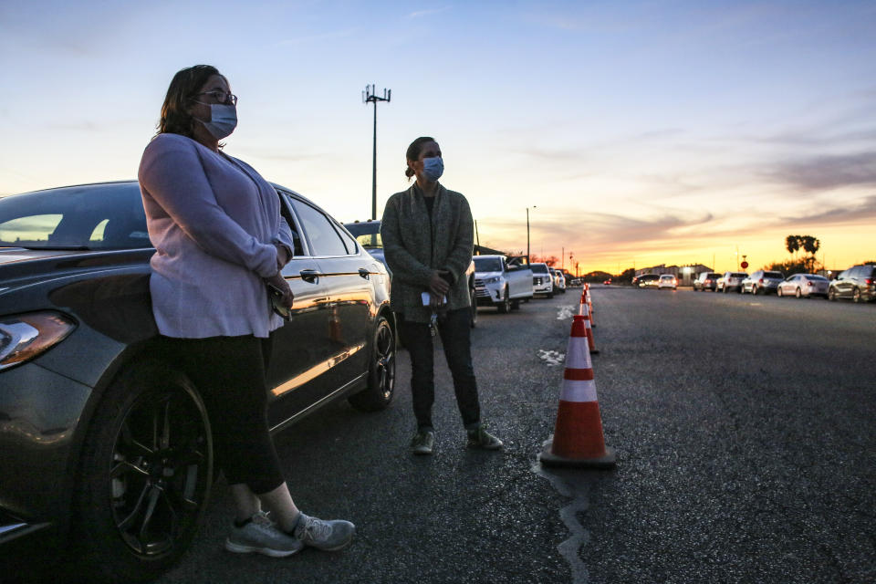 FILE - In this Thursday, Jan. 7, 2021, Cindy Rubiano and Trolena Loya stand outside their car as they wait in line overnight on behalf of their aged parents and in-laws before the COVID-19 vaccine clinic at Casa Del Sol opened on Friday morning in Harlingen, Texas. The U.S. is entering the second month of the largest vaccination effort in history with a massive expansion of the campaign, opening up football stadiums, major league ballparks, fairgrounds and convention centers to inoculate a larger and more diverse pool of people. (Denise Cathey/The Brownsville Herald via AP)