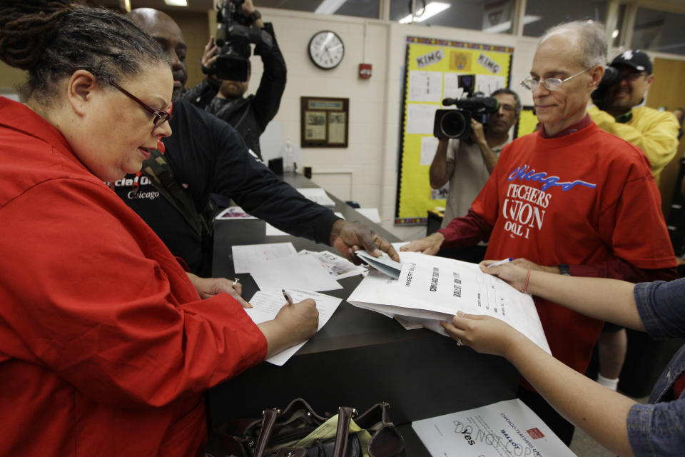 FILE - In this June 6, 2012 file photo Chicago Teachers Union President Karen Lewis, left, registers for her ballot during a strike authorization vote at a high school in Chicago. Chicago Mayor Rahm Emanuel last week announced an agreement with several unions to help bail out the nation’s worst-funded city pension systems, a festering problem inherited from his predecessor, Richard M. Daley. Emanuel said the deal, which would slice Chicago’s nearly $20 billion shortfall in half by cutting benefits and raising property taxes, would keep the funds from insolvency and avoid massive cuts in services and a record tax hike. Among its opponents is Lewis who calls the pension plan “criminal” and “just awful,” saying it will hit school employees _ who don’t receive Social Security and are predominantly women of color _ with both a loss of benefits and, for those who own homes, a property tax increase they can’t afford to pay. (AP Photo/M. Spencer Green,File)