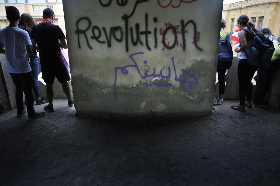 Anti-government protesters stand inside the Opera building, as they watch other protesters in front the government palace, in downtown Beirut, Lebanon, Sunday, Oct. 20, 2019. Lebanon is bracing for what many expect to be the largest protests in the fourth day of anti-government demonstrations. Thousands of people of all ages were gathering in Beirut's central square Sunday waving Lebanese flags and chanting the "people want to bring down the regime." Arabic center reads, "We are coming." (AP Photo/Hussein Malla)