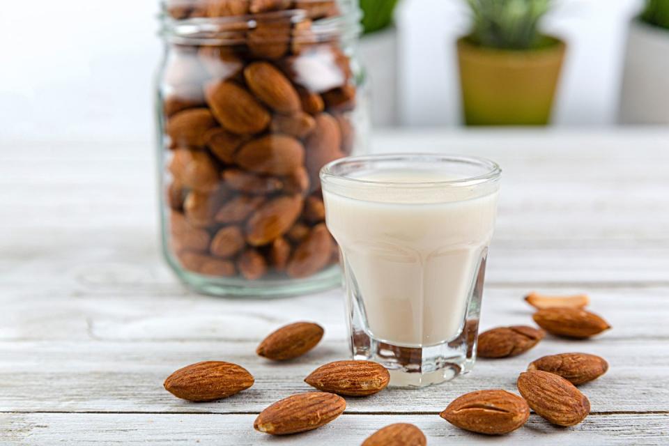 raw almonds in a jar, a glass of almond milk, and a few of raw almonds scattering on the table