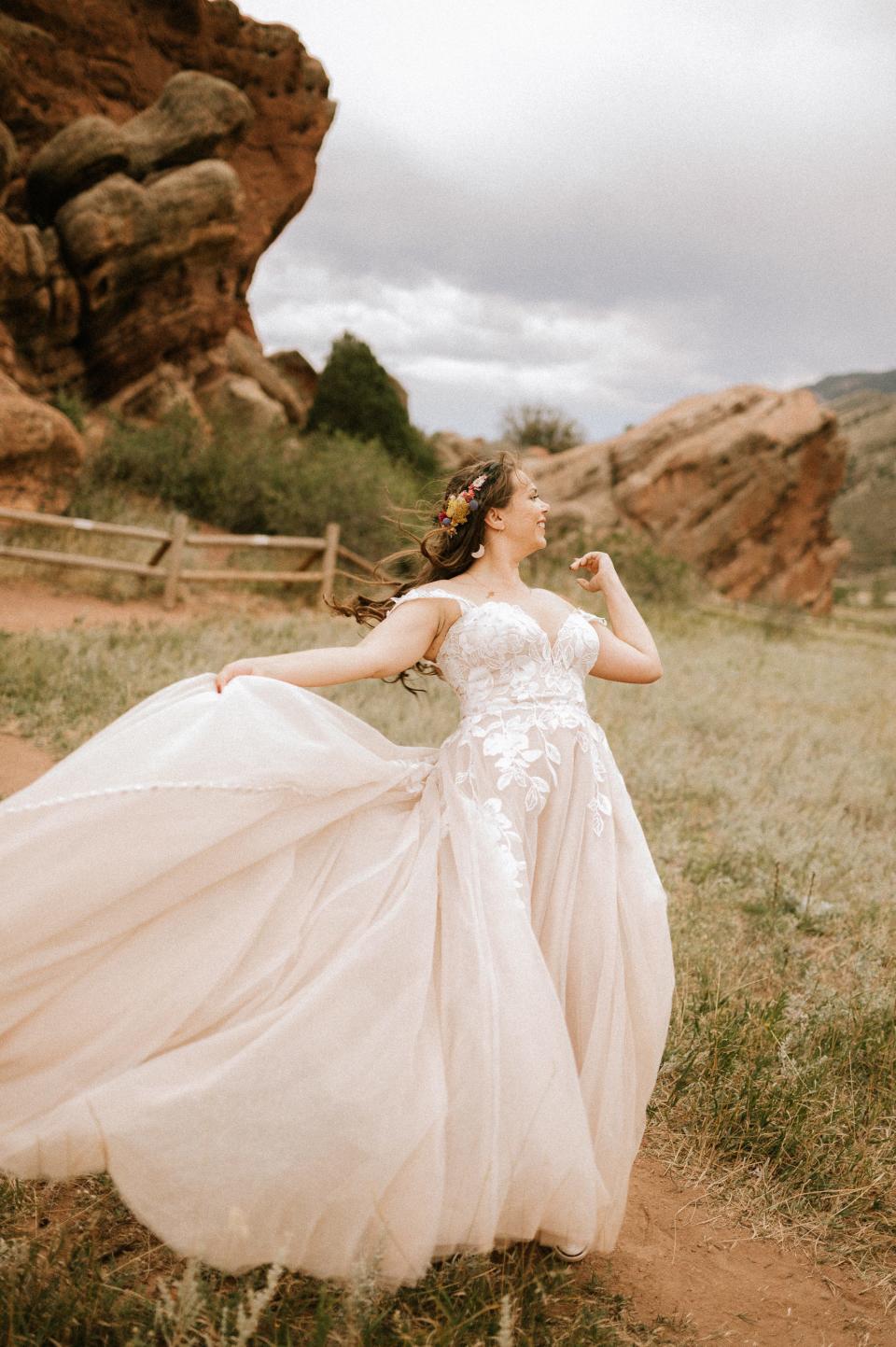 A bride stands in her wedding dress in a field as it blows in the wind.