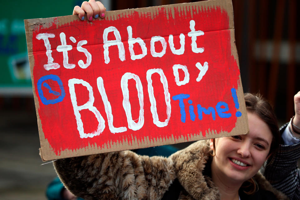 A woman holding up a sign that says "It's about bloody time"