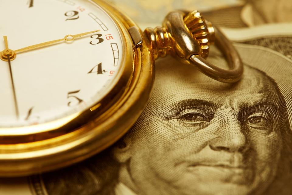 A close-up of a $100 bill, with a pocket watch next to it.