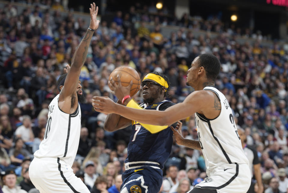 Denver Nuggets guard Reggie Jackson, center, drives to the basket between Brooklyn Nets forward Royce O'Neale, left, and center Nic Claxton in the second half of an NBA basketball game Sunday, March 12, 2023, in Denver. (AP Photo/David Zalubowski)